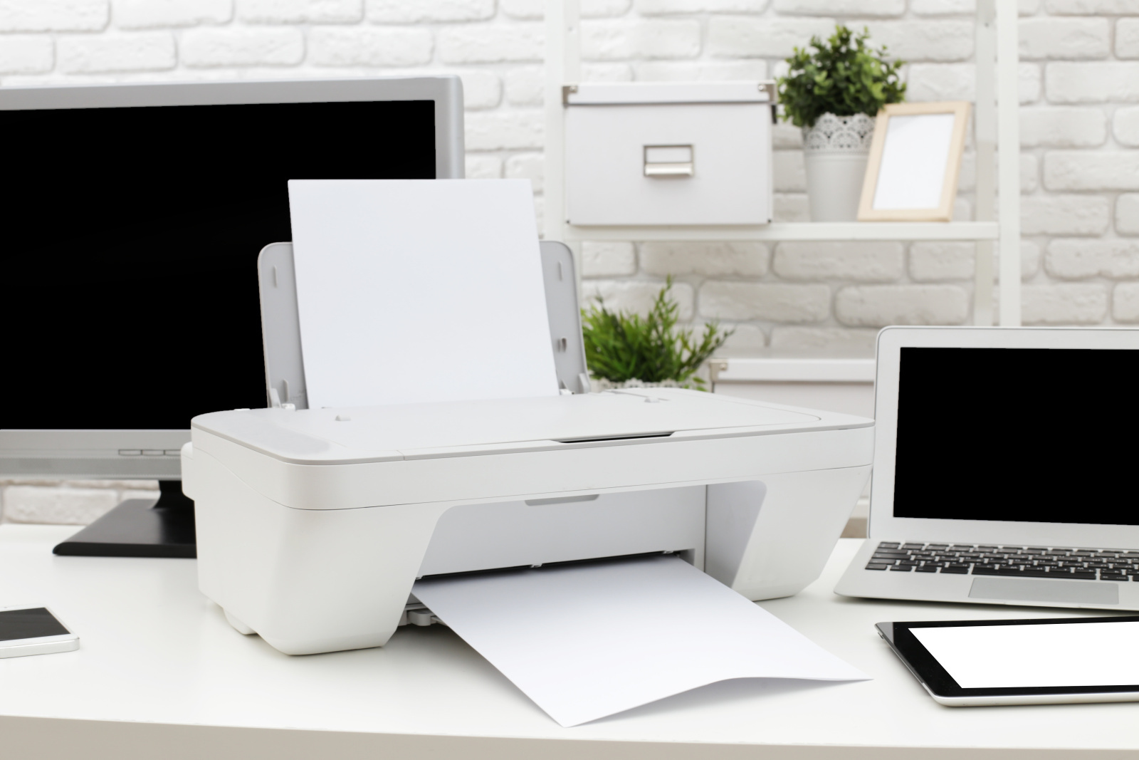 Tiskárna s xeroxovým papírem vedle notebooku.